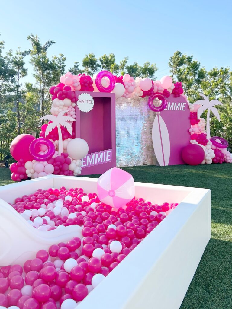 Pink ball pit with balloon backdrop at an outdoor party